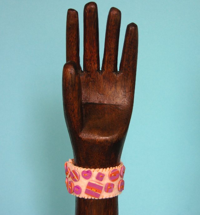 peach felt cuff shown on a wooden hand with pink and orange streaked buttons
